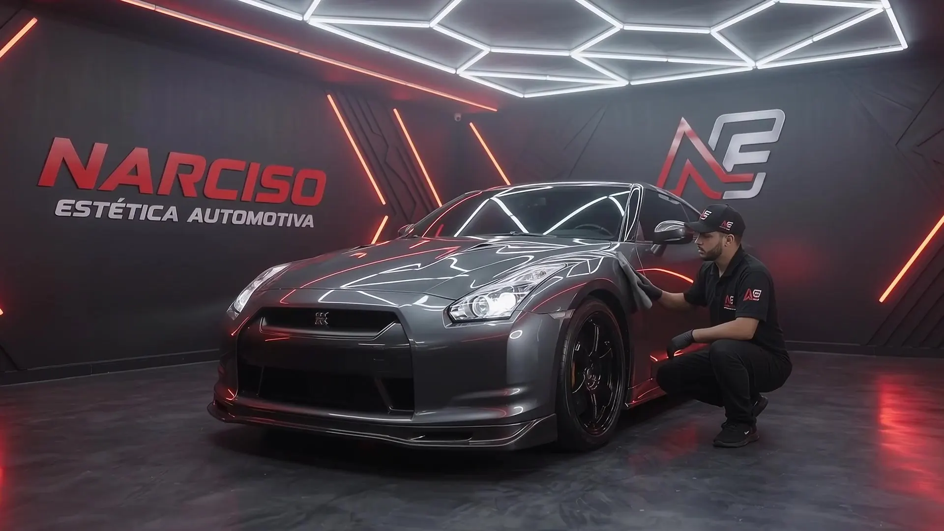 Carro esportivo cinza recebendo acabamento em ambiente de estética automotiva com iluminação vermelha